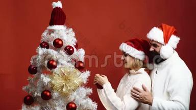 可爱的一对幸福的夫妇在圣诞树旁迎接新年。 一对年轻夫妇戴着新年`帽子装饰圣诞节